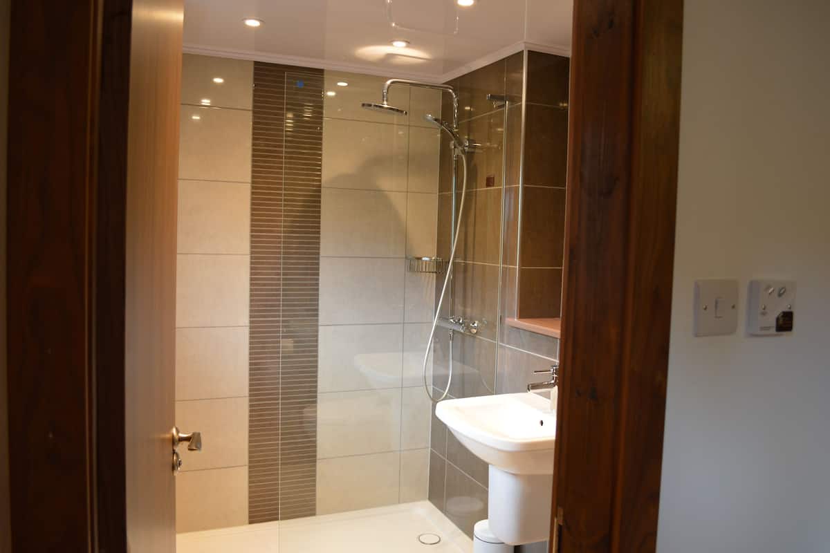A modern bathroom with a glass shower enclosure, a white sink, and wooden paneling.