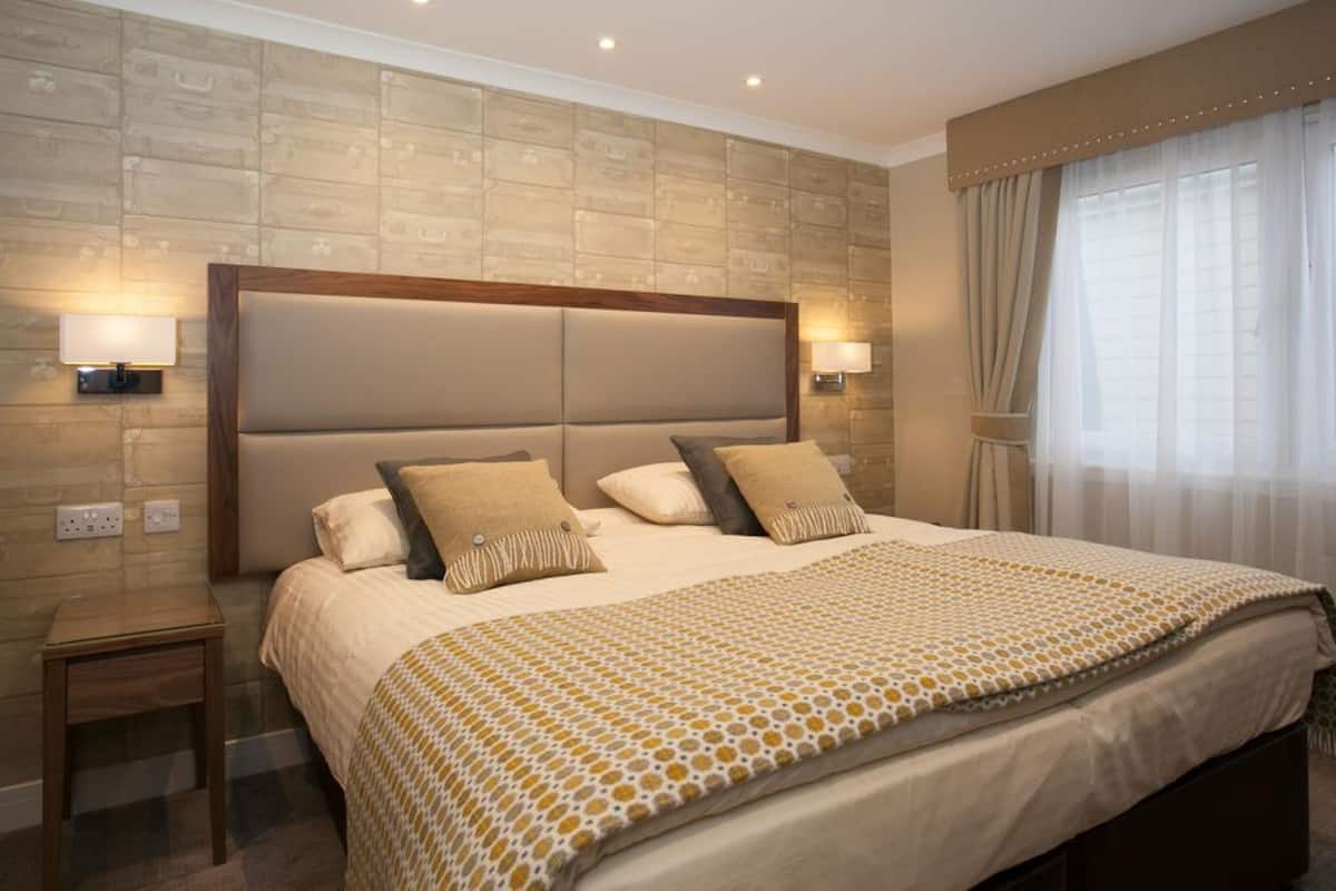 A hotel room with a large bed, two bedside lamps, a nightstand, and a window with curtains.