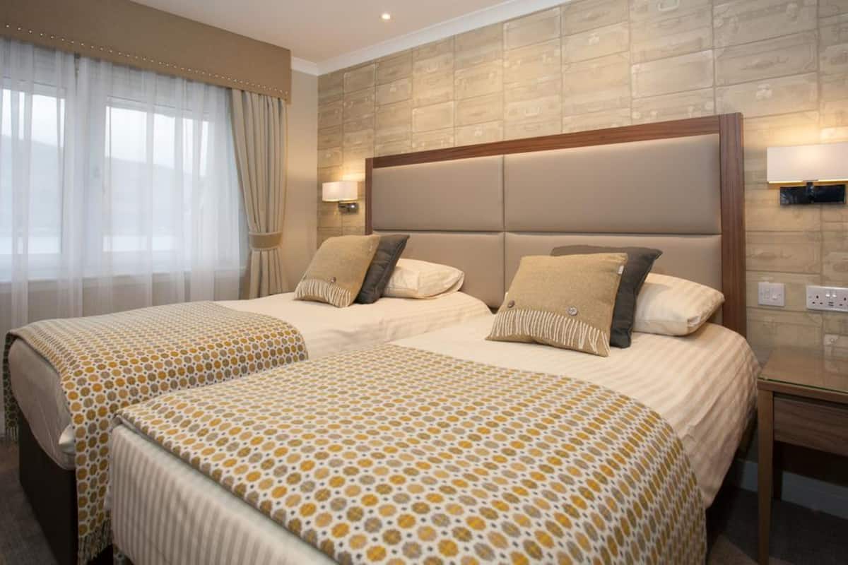 A hotel room with two beds, each with a headboard, a bedside table, and a lamp.