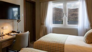A hotel room with a bed, a desk, a chair, a television, and a window with a view of hills and water. - Cruachan Hotel (Fort William)
