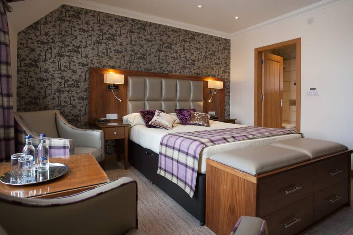 A hotel room with a large bed, a bedside table with lamps, a chair, and a small table with a tray.