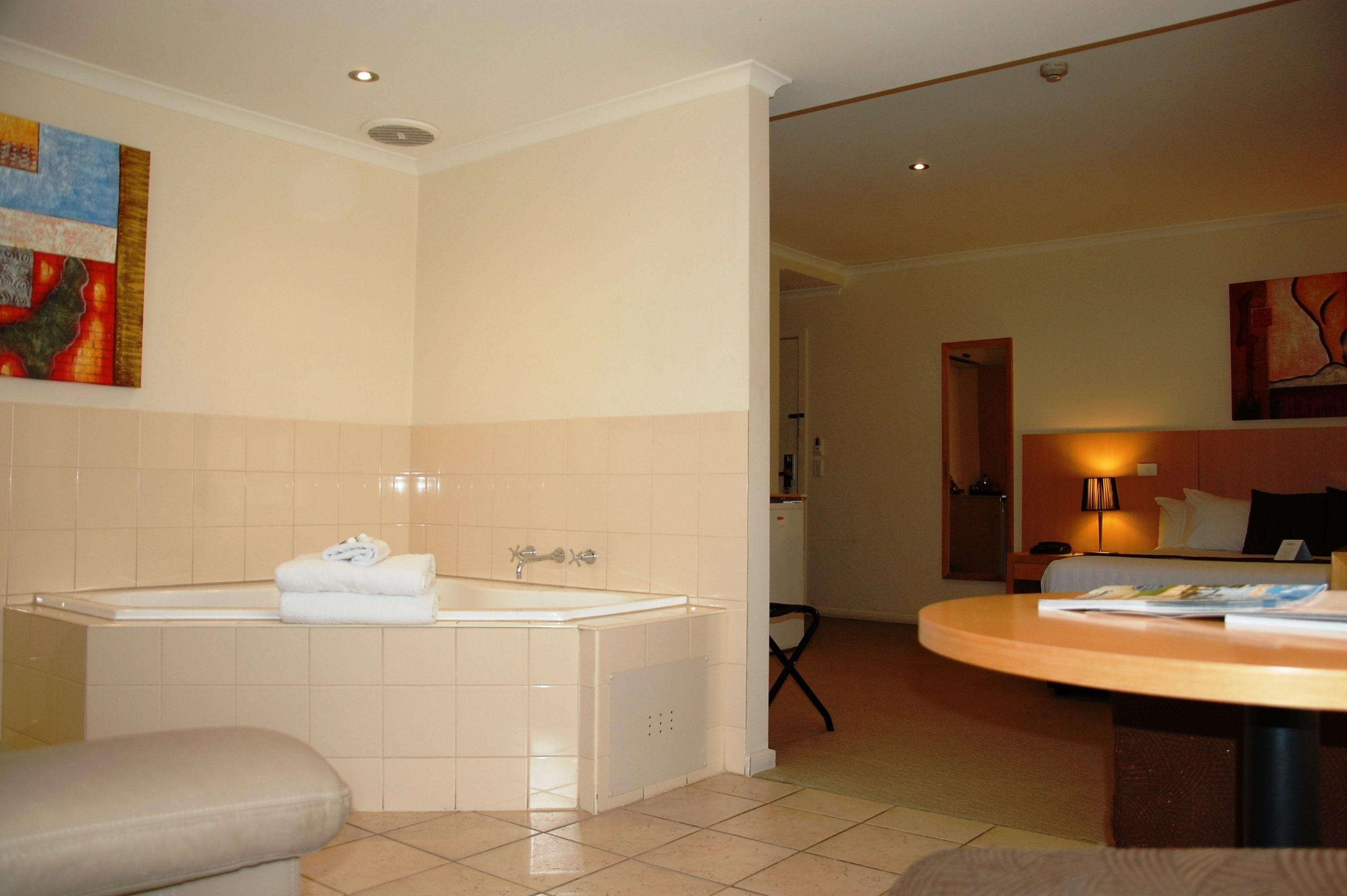 A hotel bathroom with a bathtub, a sink, and a toilet. There is a painting on the wall and a lamp in the room.
