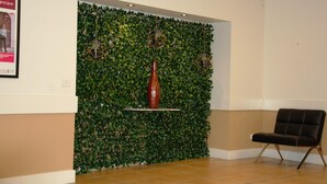 Un hall d’entrée avec un mur vert, un vase rouge et un fauteuil noir.