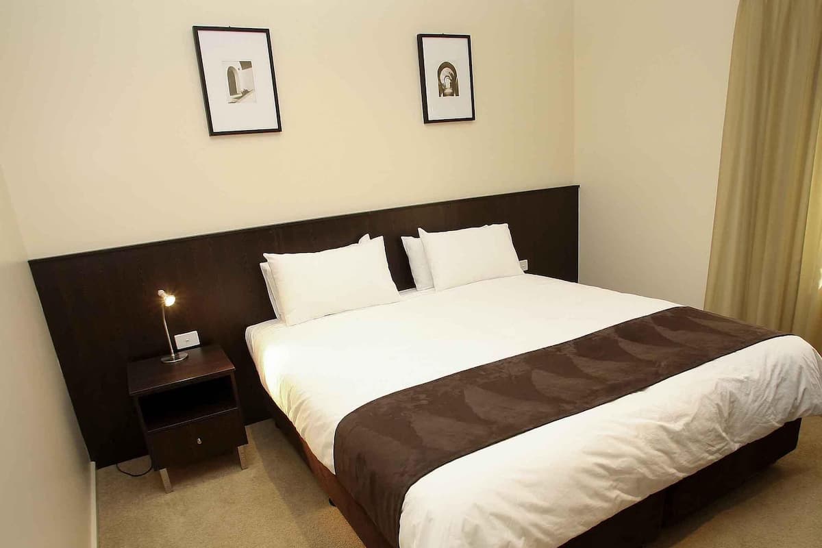 Ein Hotelzimmer mit einem großen Bett, zwei Nachttischen, einem Beistelltisch und zwei gerahmten Bildern an der Wand.