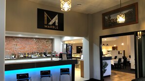 Un espace bar agrémenté d’une enseigne en marbre, d’un mur en briques et d’un coin salon avec des tabourets.