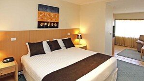Une chambre d’hôtel avec un grand lit, une table de chevet, une lampe, une chaise et un tableau au mur.