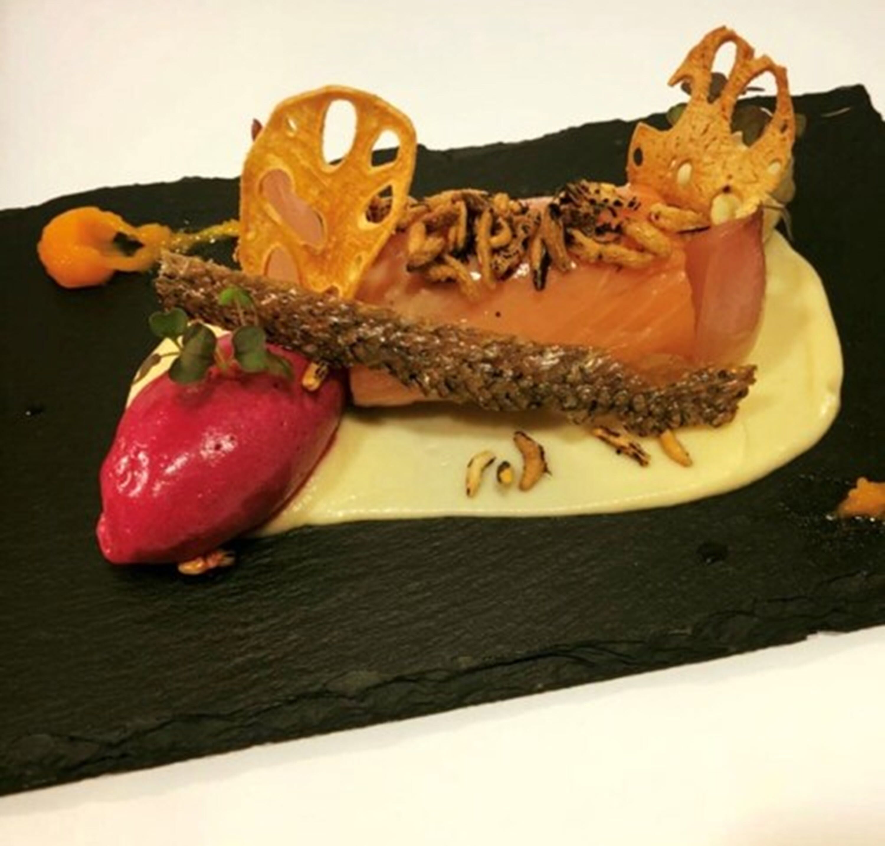 Ein Desserteller mit einem Lachsfilet, einer Erdbeere und dekorativen Elementen.