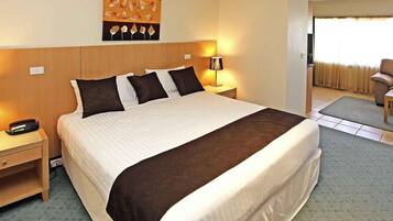 A hotel room with a large bed, a bedside table, a lamp, a chair, and a painting on the wall.