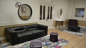 Une pièce comprenant un canapé en cuir noir, deux poufs ronds, une petite table et un tapis à motifs.