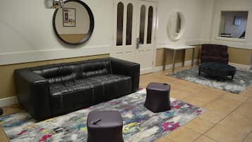 A room with a black leather sofa, two round ottomans, a small table, and a patterned rug.
