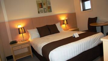 A neatly made bed with a brown and white striped bedspread, two bedside lamps, a small table with a chair, and a wall art piece above the bed.
