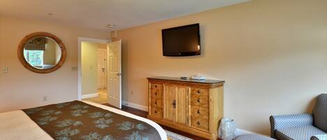 A bedroom with a bed, dresser, TV, and two armchairs.