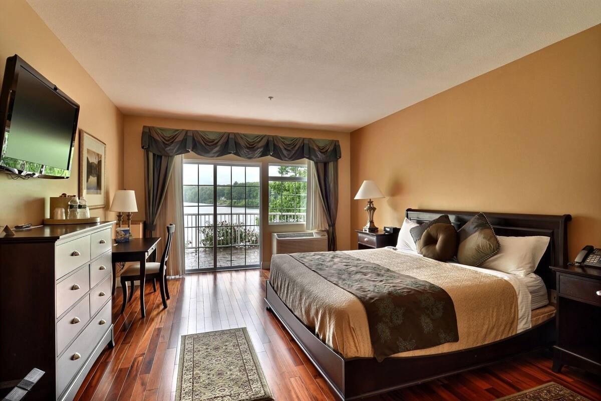 A hotel room with a bed, a desk, a chair, a TV, a window with a view, and a balcony.