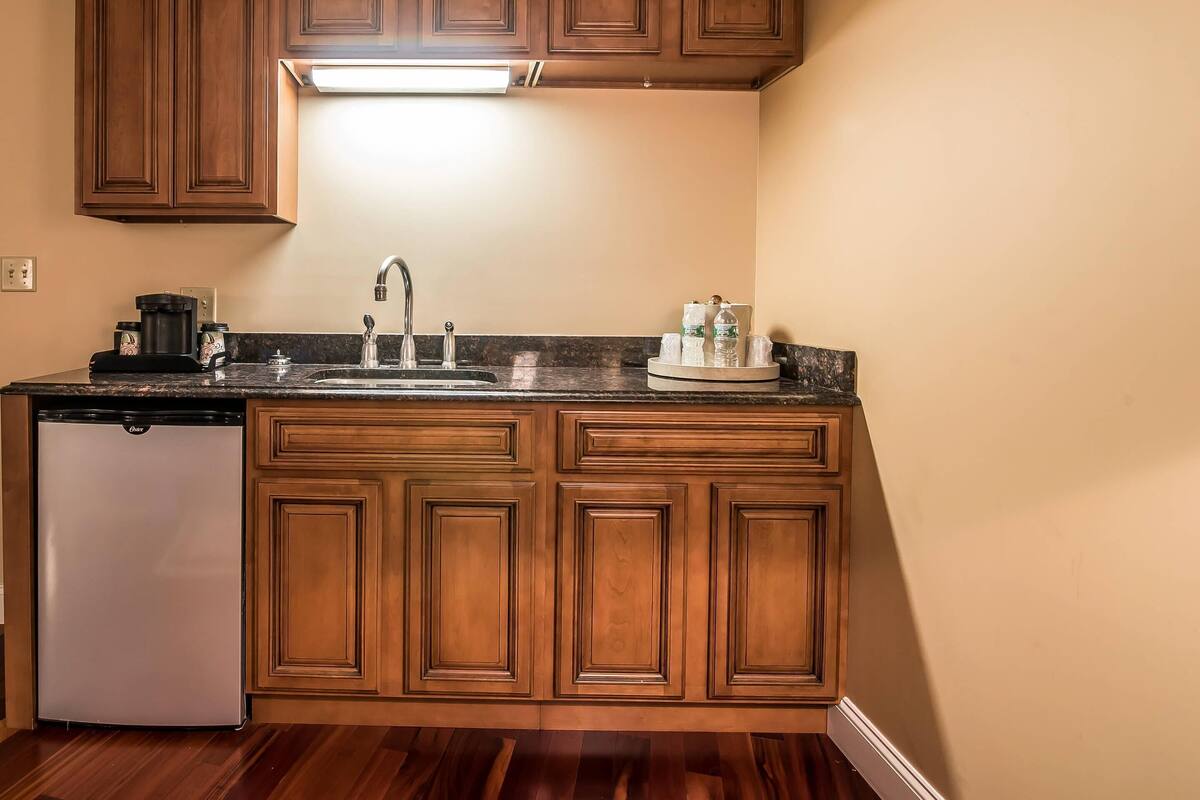 A kitchen with wooden cabinets, a stainless steel refrigerator, a sink, and a countertop with a coffee maker and glassware.