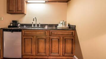 Una cocina con armarios de madera, un refrigerador de acero inoxidable, un lavamanos y una encimera con una cafetera y cristalería.