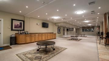 A spacious hotel lobby with a long reception desk, multiple tables, and a large rug.