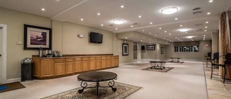 A spacious hotel lobby with a long reception desk, multiple tables, and a large rug.