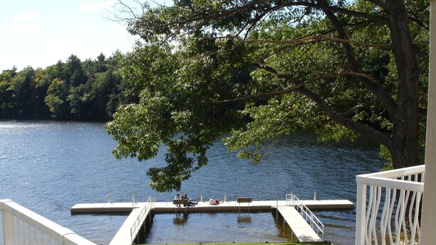 Une jetée qui s’avance dans un lac, avec une zone herbeuse au premier plan et des arbres en arrière-plan.