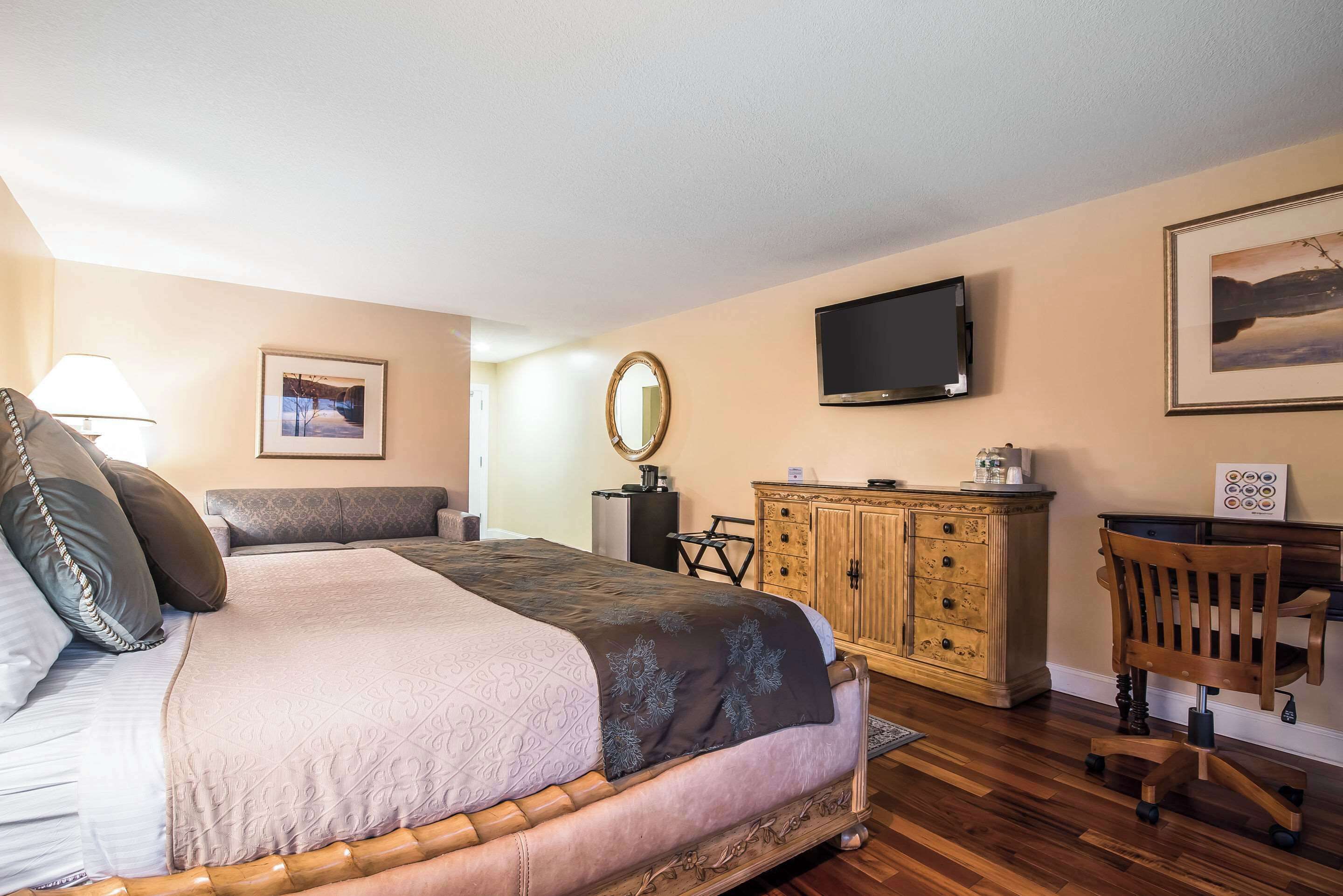 A bedroom with a large bed, a wooden dresser, a desk, a chair, a television, and a framed picture on the wall.