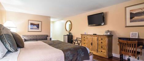 A bedroom with a large bed, a wooden dresser, a desk, a chair, a television, and a framed picture on the wall.