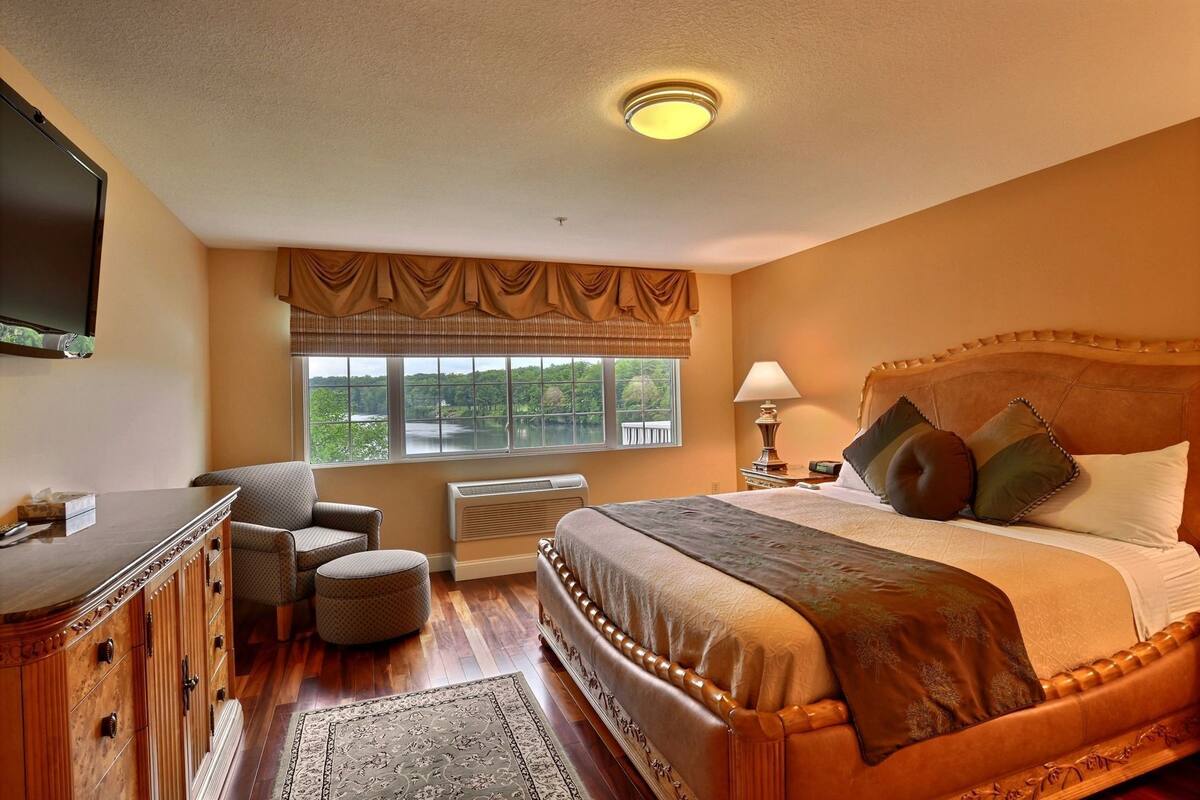 A bedroom with a bed, a desk, a chair, a window with a view, and a ceiling light.