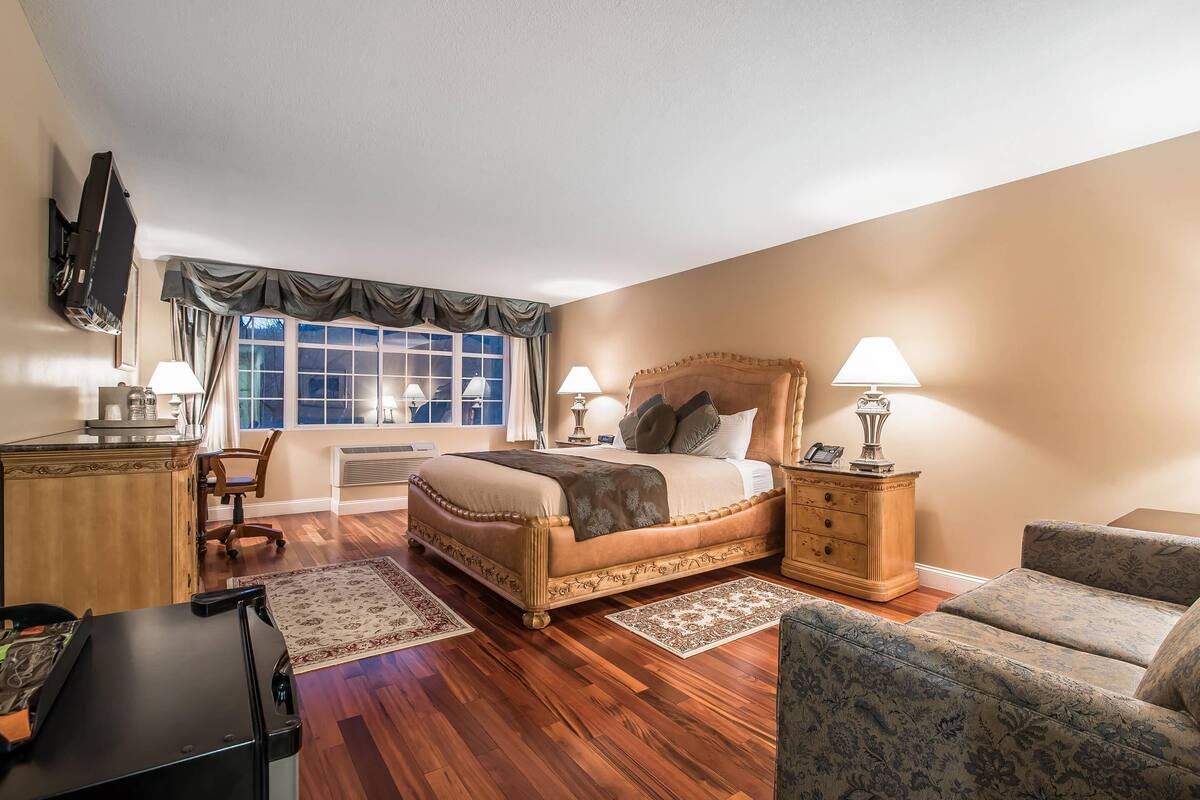 A hotel room with a large bed, a desk, a chair, a sofa, and a TV.