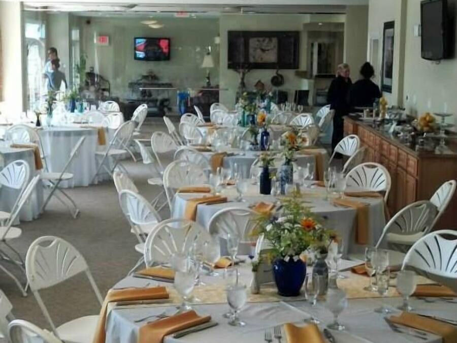 A banquet hall with round tables set for dining, white chairs, and overhead lighting.