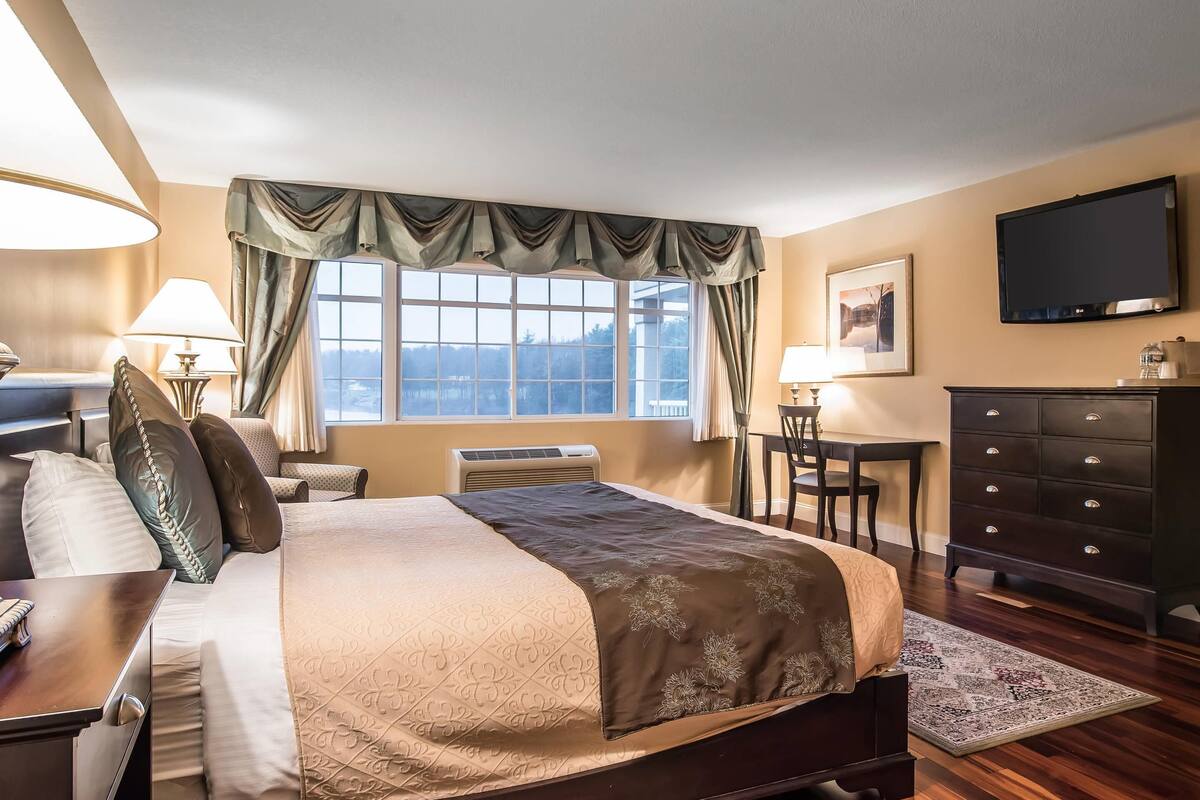 A hotel room with a bed, a desk, a chair, a dresser, and a TV.