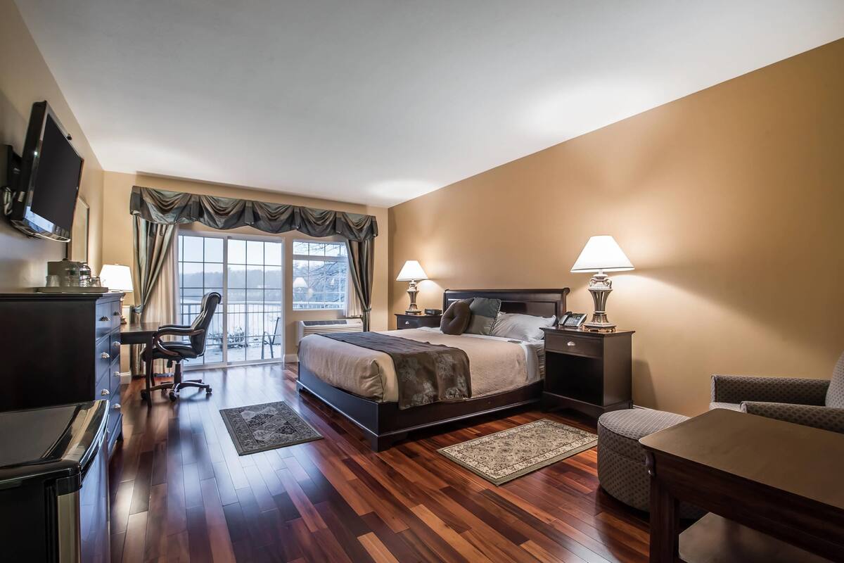 A hotel room with a large bed, a desk, a chair, a TV, and a window with curtains.