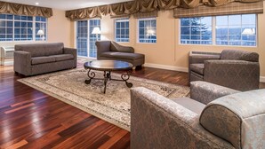 Un salon spacieux doté d’une grande fenêtre, d’un tapis à motifs et de plusieurs options d’assises, notamment un canapé et des fauteuils.