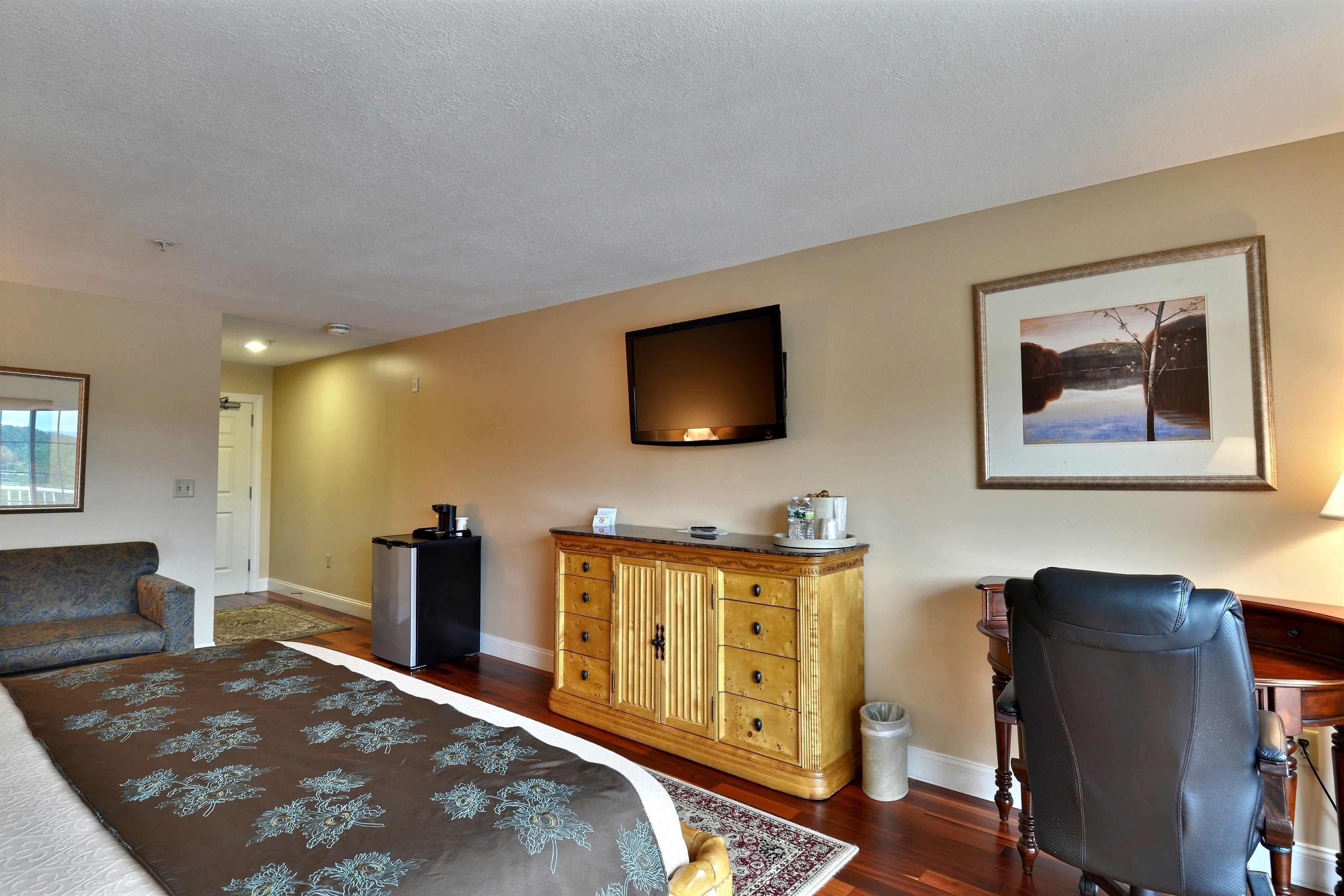A hotel room with a bed, a desk, a chair, a television, and a framed picture on the wall.