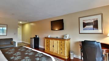 A hotel room with a bed, a desk, a chair, a television, and a framed picture on the wall.