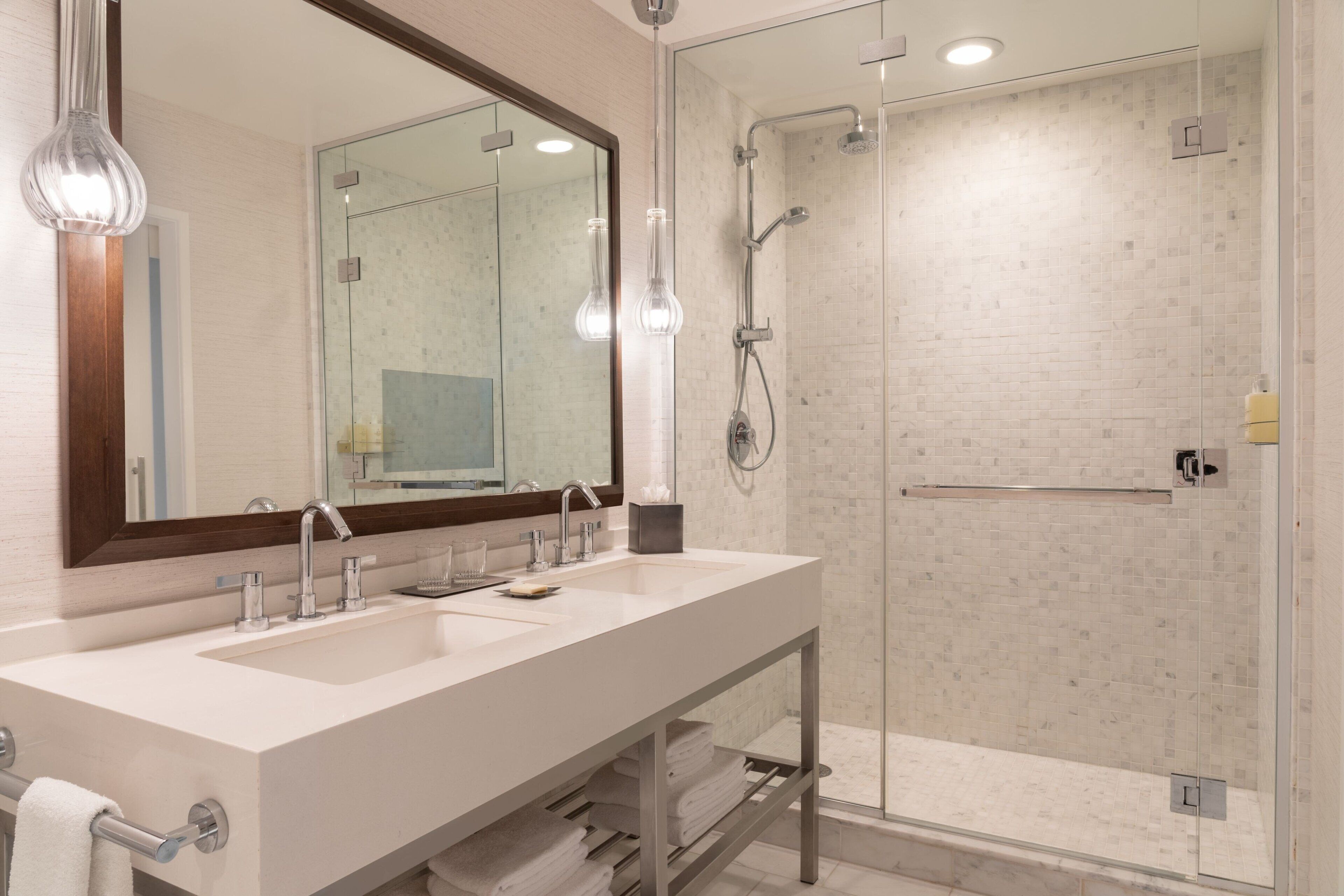 A modern bathroom with two sinks, a large mirror, and a glass-enclosed shower area.