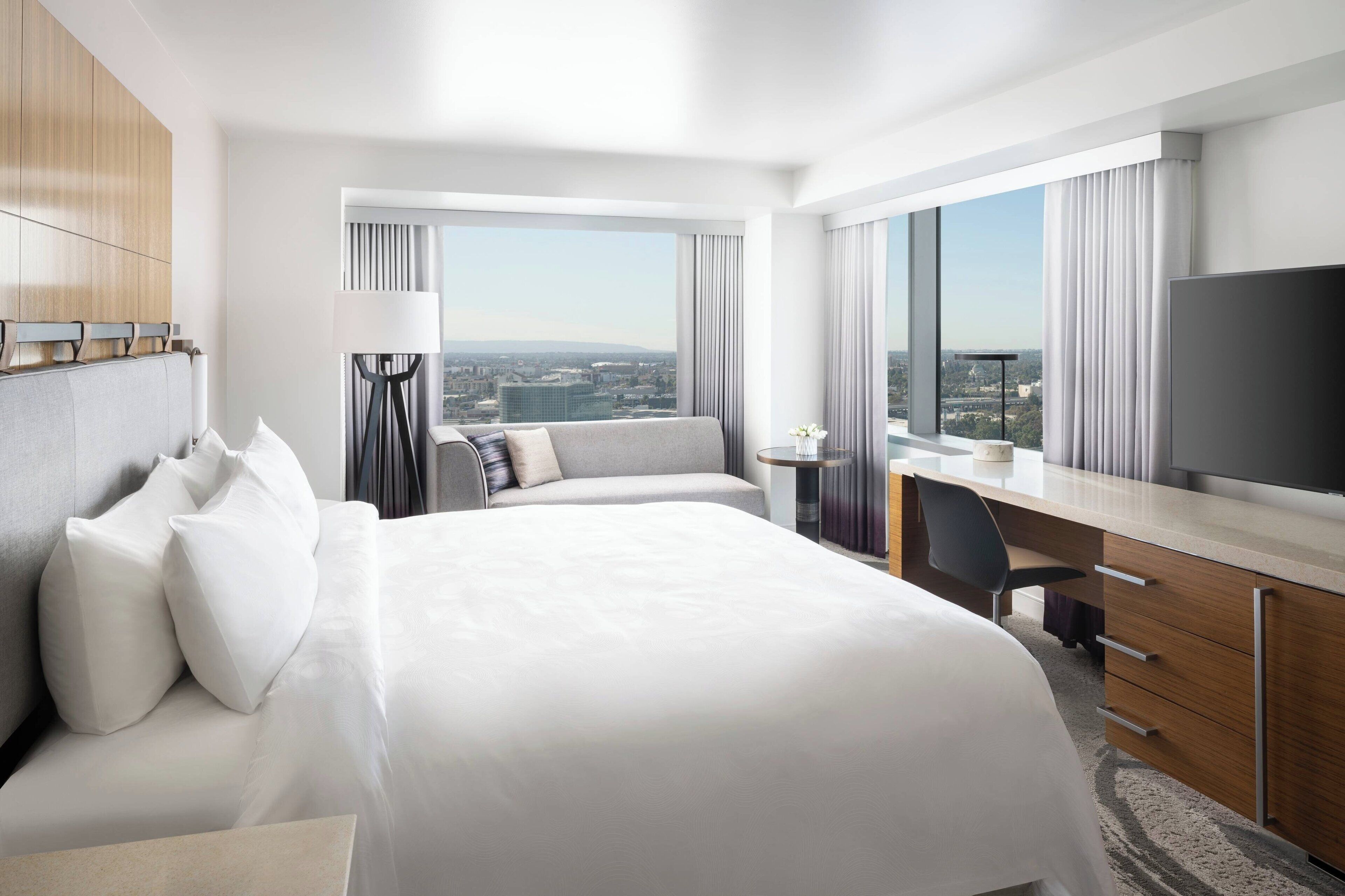 A hotel room with a large bed, a desk, and a view of the city.