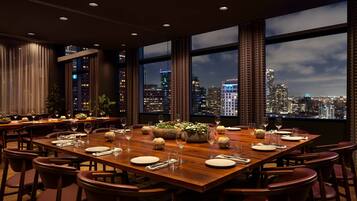 Comedor con vista a la ciudad, ventanas amplias y mesa de madera dispuesta para una comida.