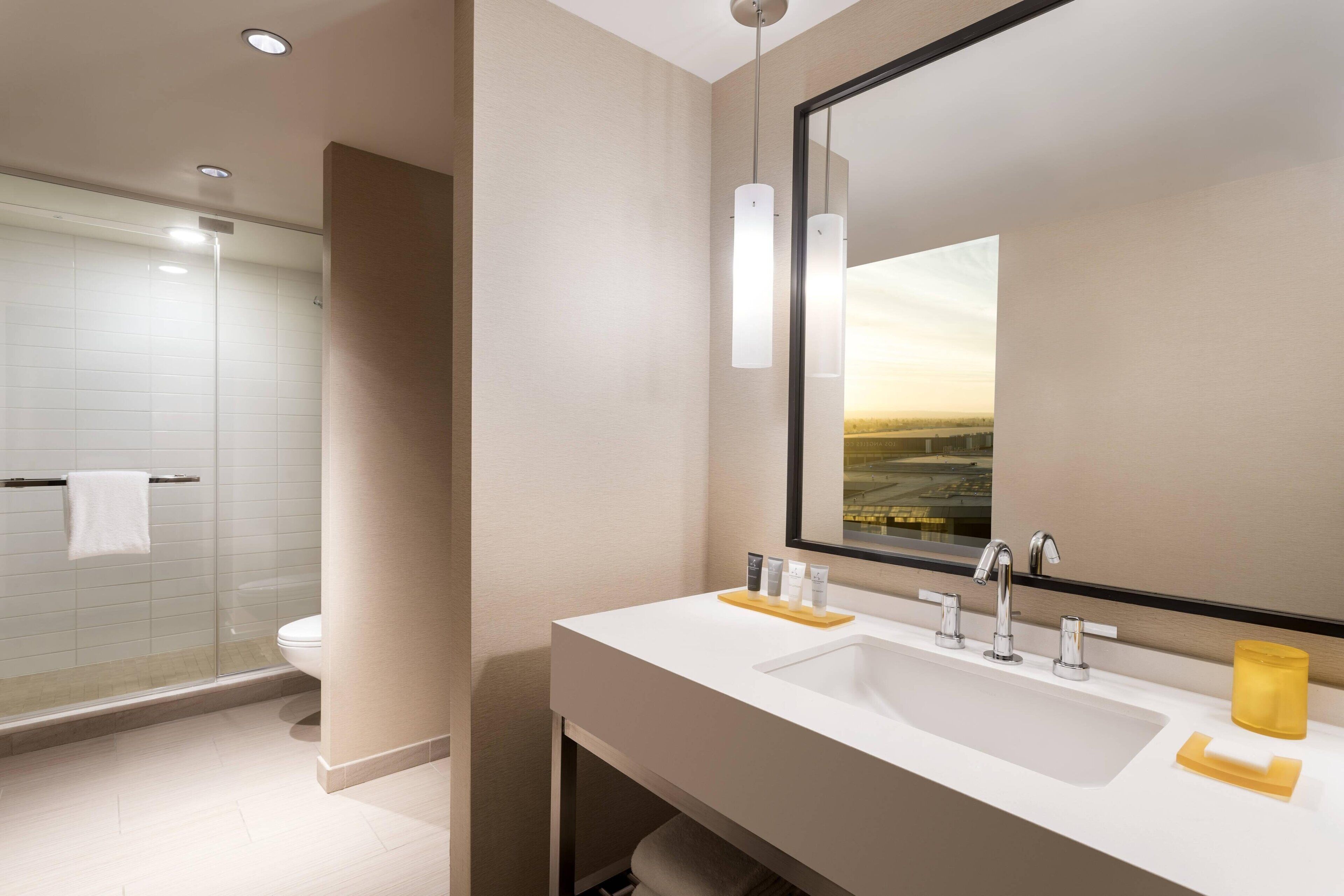 A modern bathroom with a large mirror, two sinks, and a glass shower enclosure.