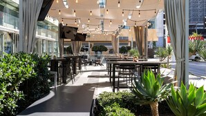 An outdoor dining area with tables and chairs, surrounded by greenery and a modern architectural setting. - JW Marriott Los Angeles L.A. LIVE (Los Angeles)