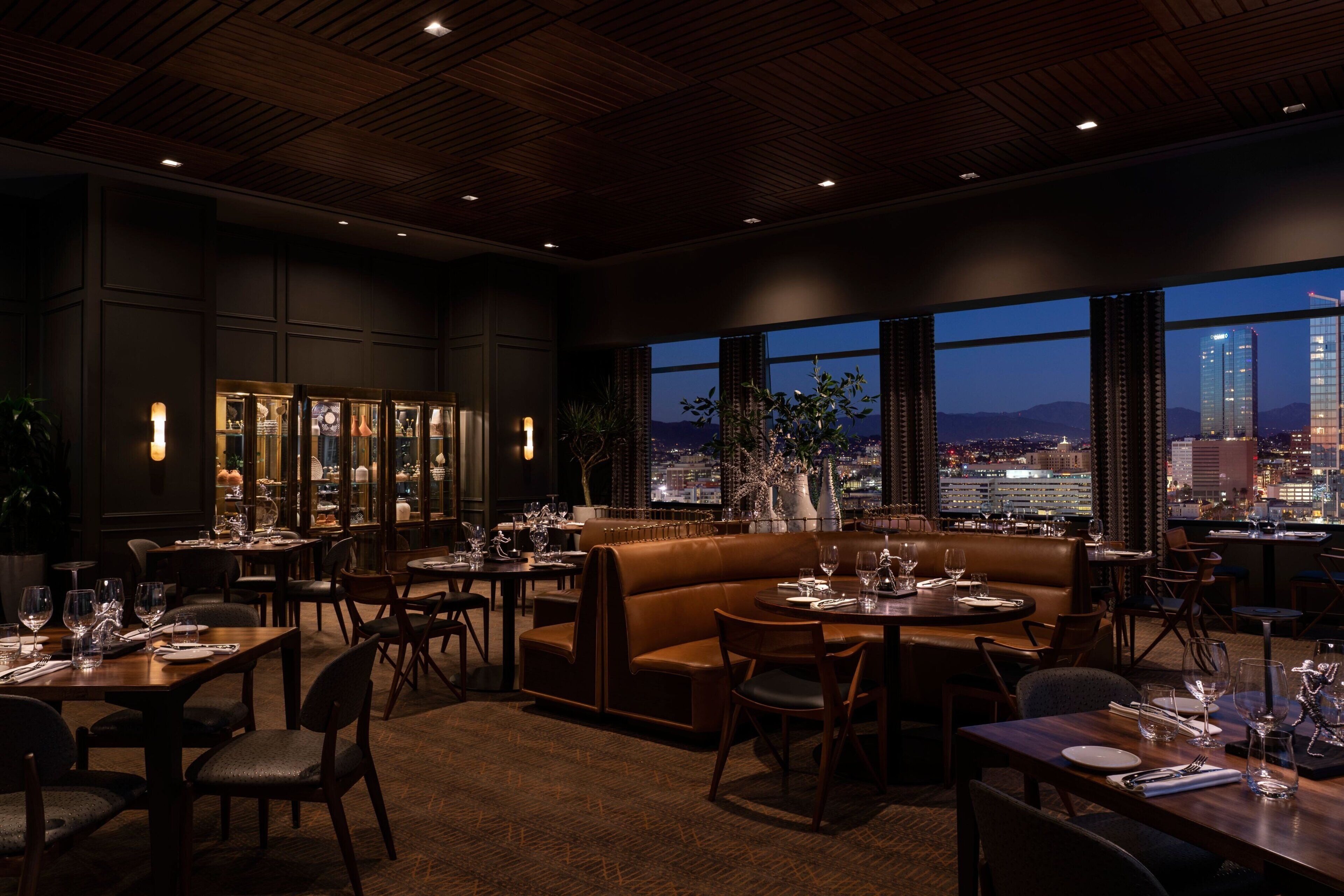 A dimly lit restaurant with a city view, featuring leather seating and a modern interior.