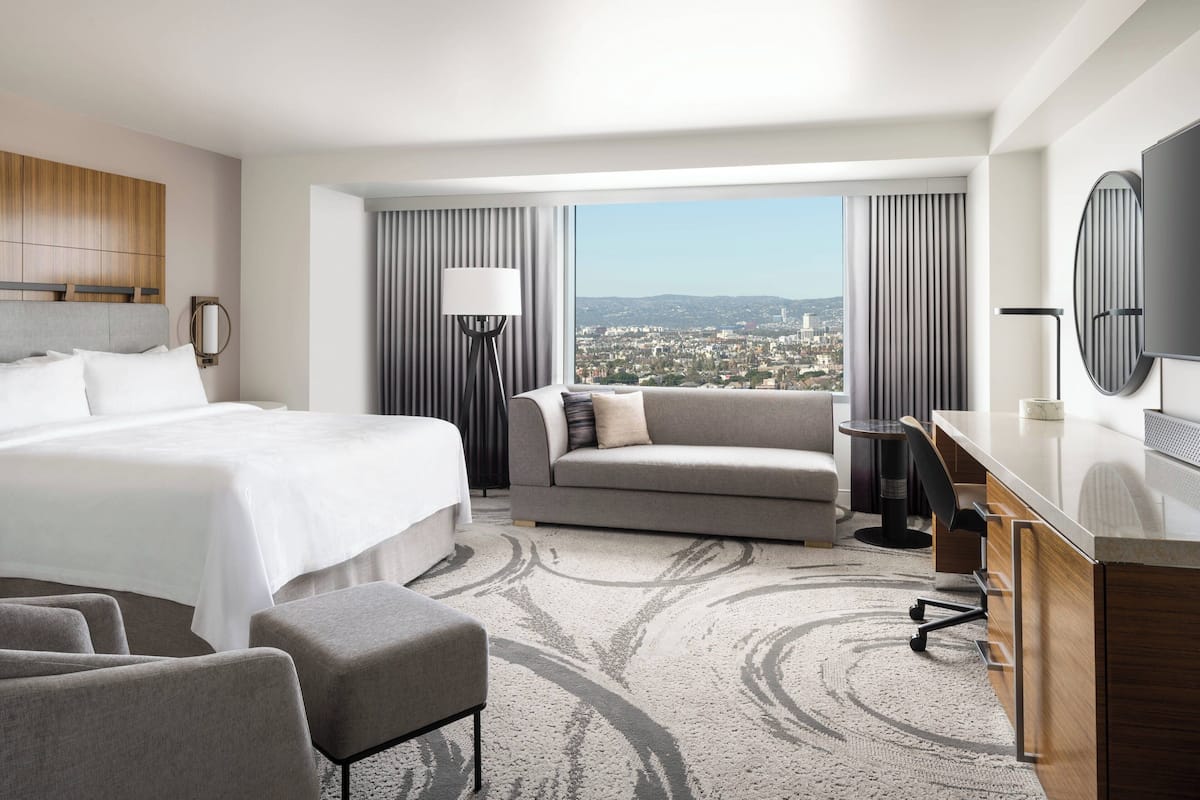 A hotel room with a large bed, a sofa, a desk, and a view of the city.