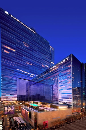 Un hotel JW Marriott con fachada de vidrio moderna, piscina exterior e iluminación destacada.