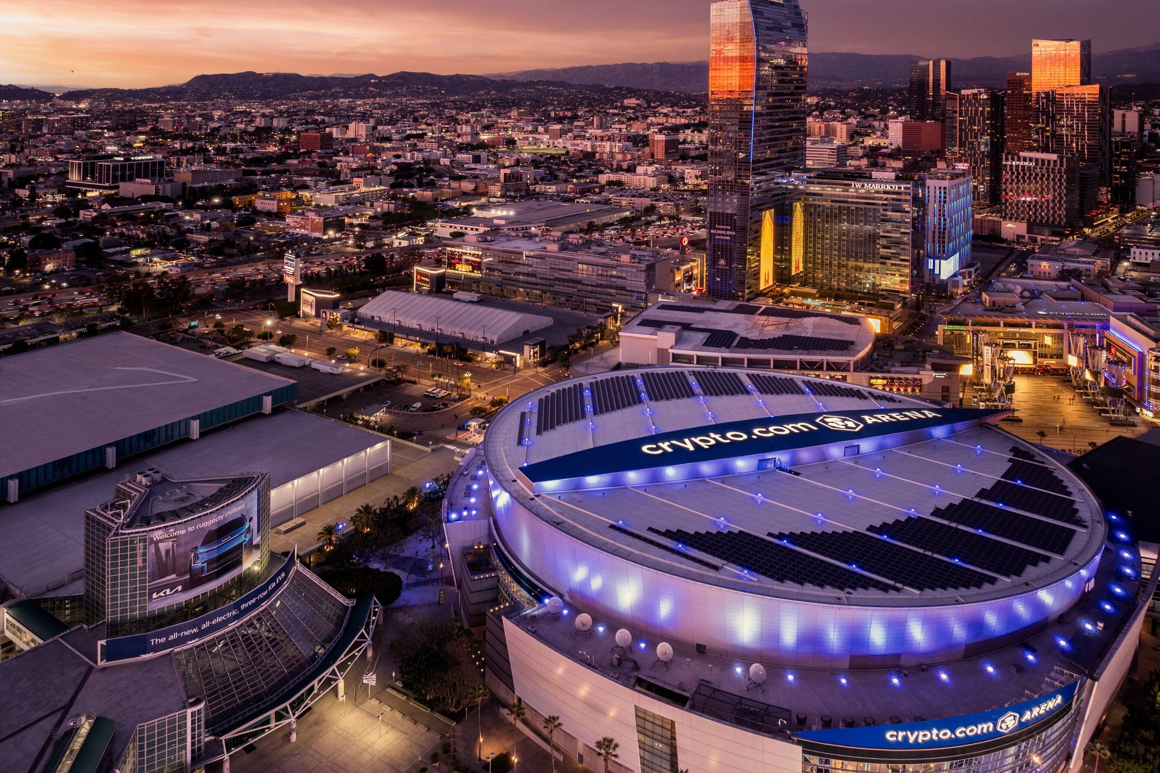 A large, modern stadium with a Crypto.com Arena sign, surrounded by urban buildings and a cityscape at dusk.