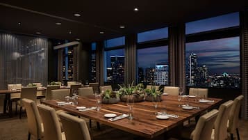Comedor con una gran mesa de madera dispuesta para seis personas, rodeada de sillas y vistas panorámicas de la ciudad a través de amplios ventanales.