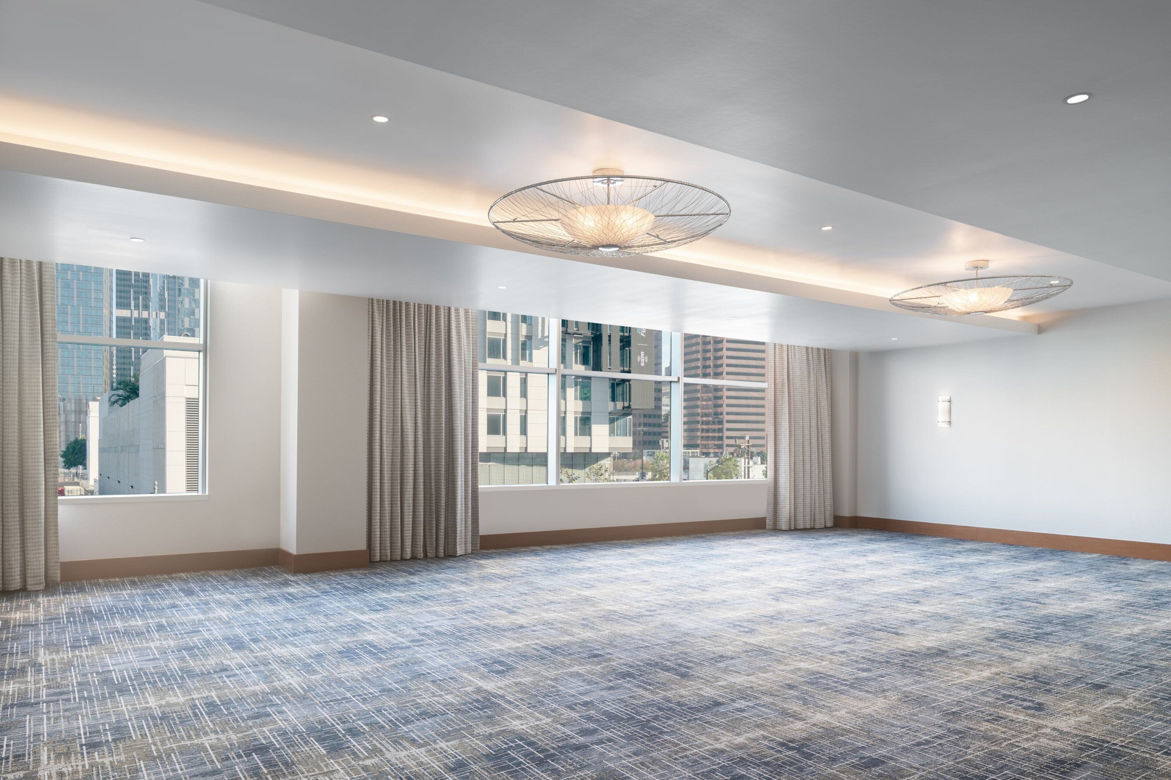 A spacious hotel room with large windows, a patterned carpet, and modern pendant lighting.