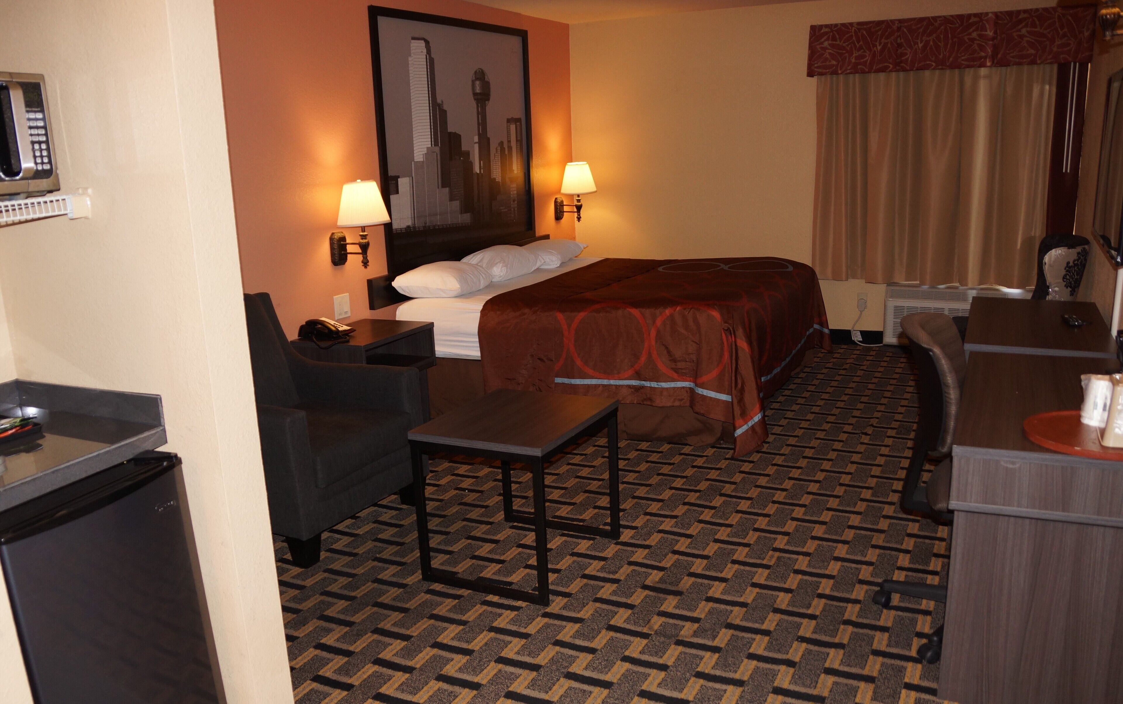 Quarto de hotel com cama, duas mesas de cabeceira, escrivaninha, cadeira, micro-ondas e telefone.