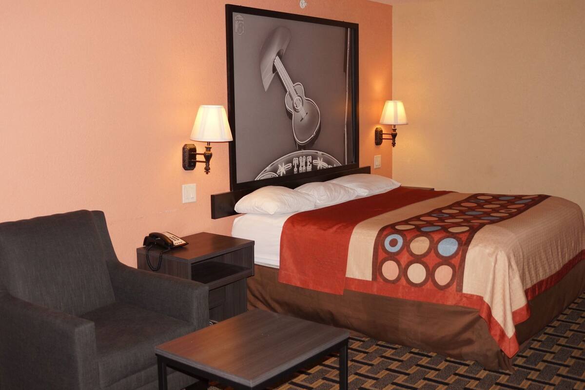 Habitación de hotel con una cama, una silla, una mesita, un teléfono y dos lámparas de pared.