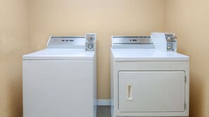 Twee gestapelde wasmachines en drogers in een hoek, met beige wanden.