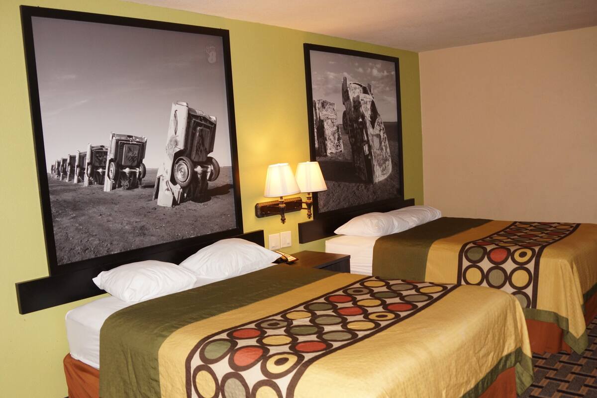 Habitación de hotel con dos camas, cada una con una colcha estampada, una mesita de noche con lámpara y dos fotografías grandes en blanco y negro en la pared.
