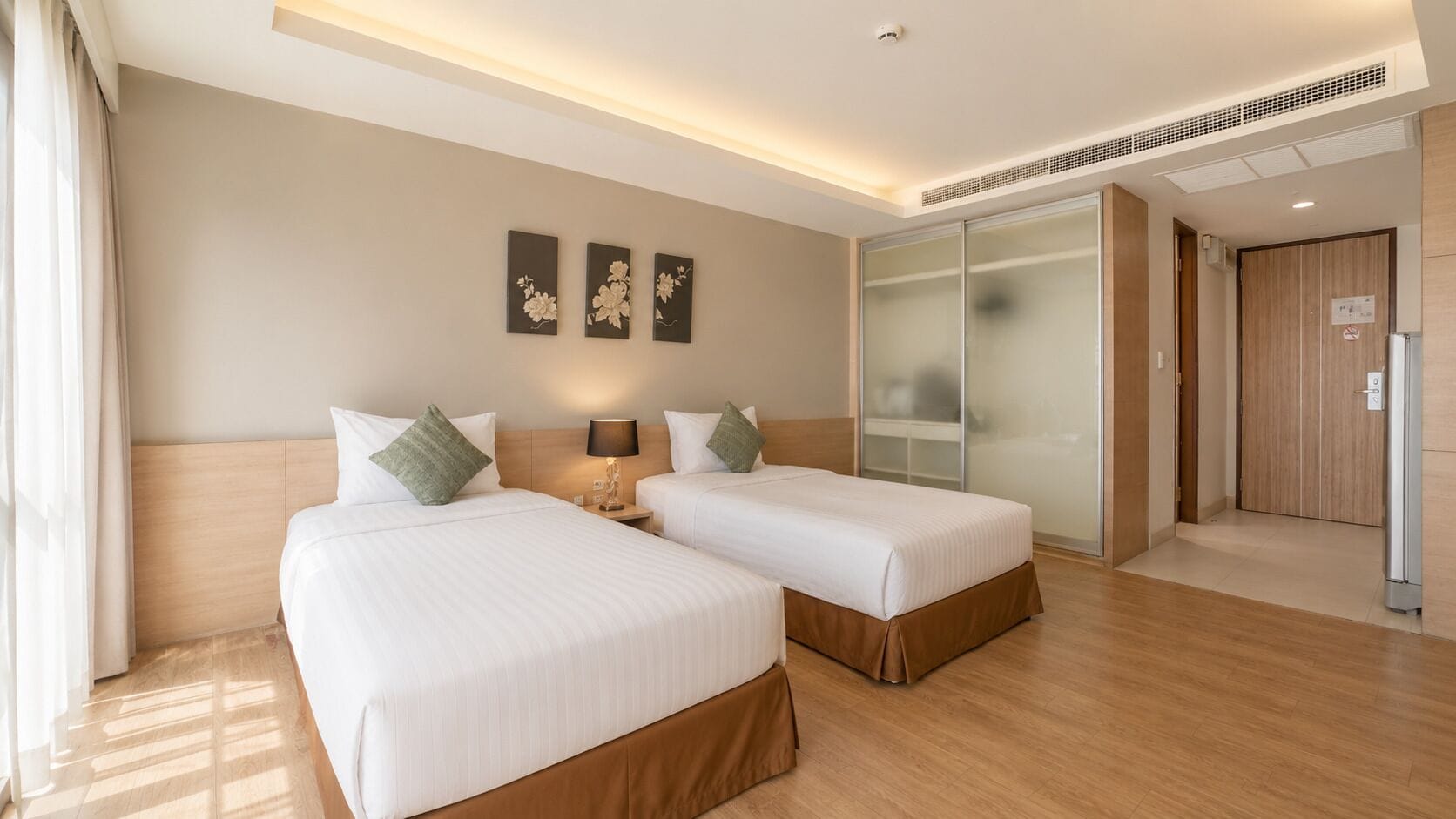 Quarto de hotel com duas camas, uma mesa de cabeceira com abajur, um guarda-roupa com portas deslizantes e uma obra de arte na parede.