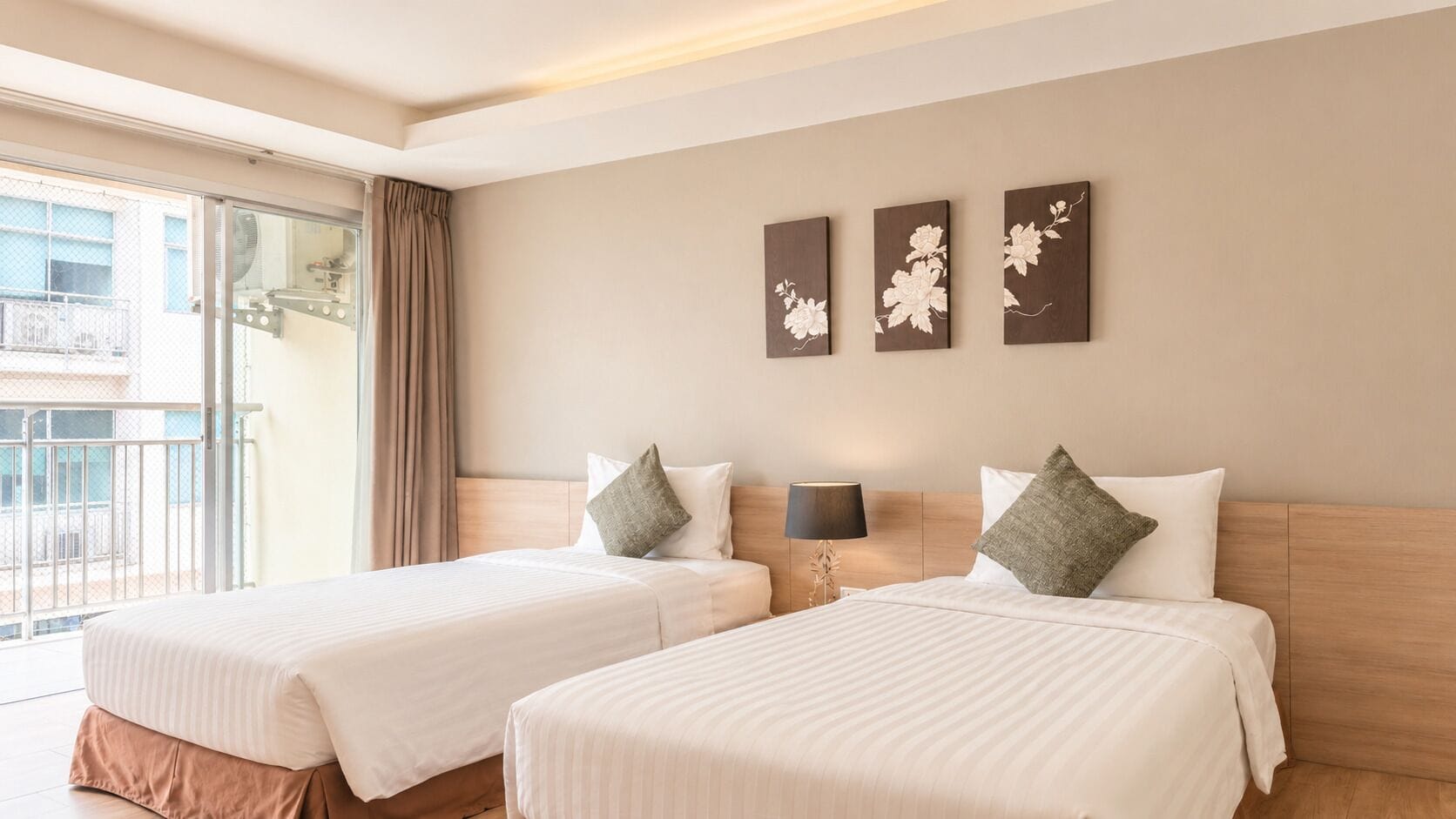Habitación de hotel con dos camas, un balcón y tres cuadros florales colgados en la pared.