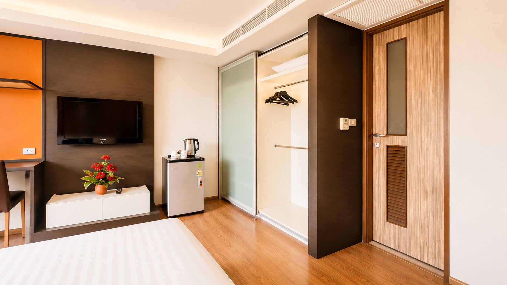 A hotel room with a bed, a TV, a mini-fridge, a coffee maker, a desk, and a wardrobe.